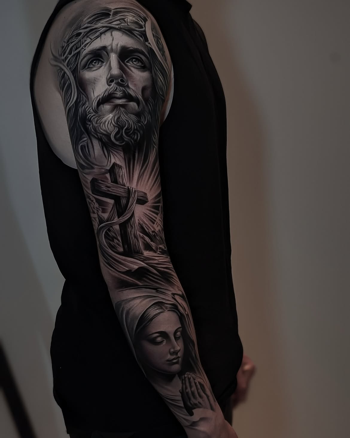 Realistic black and grey tattoo of Jesus Christ with a cross on the upper arm by Alejandro 
